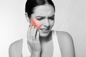 Woman grabbing her cheek in pain, in need of an emergency Dentist